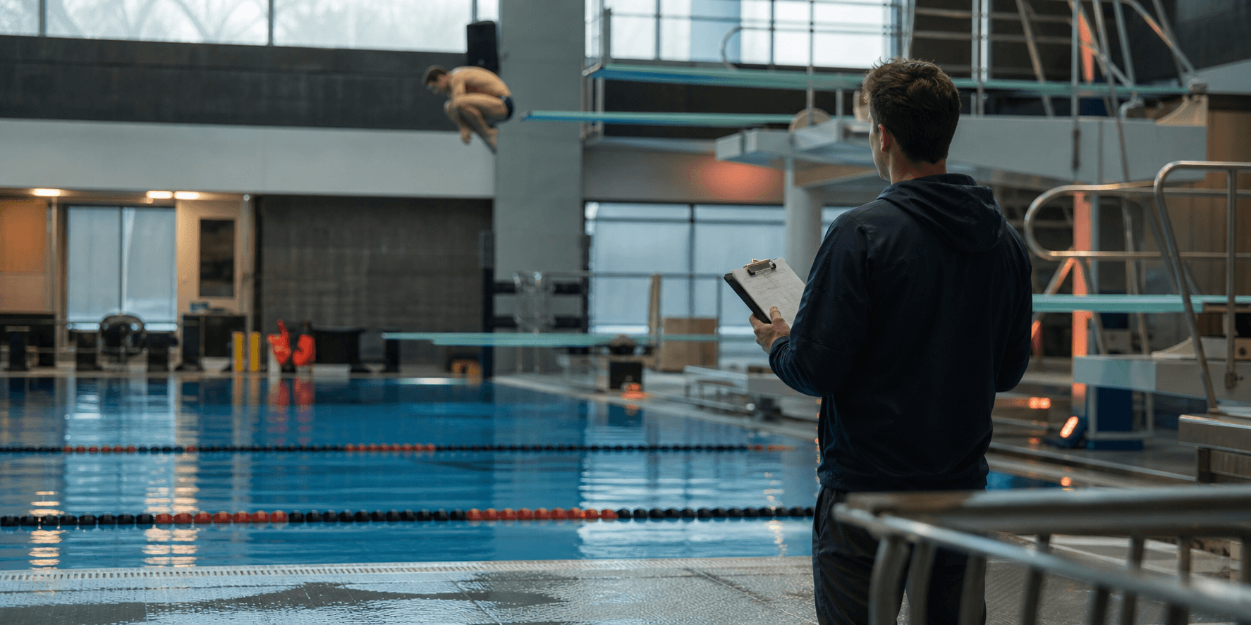 A college diving coach watching a diver practice from the pool deck